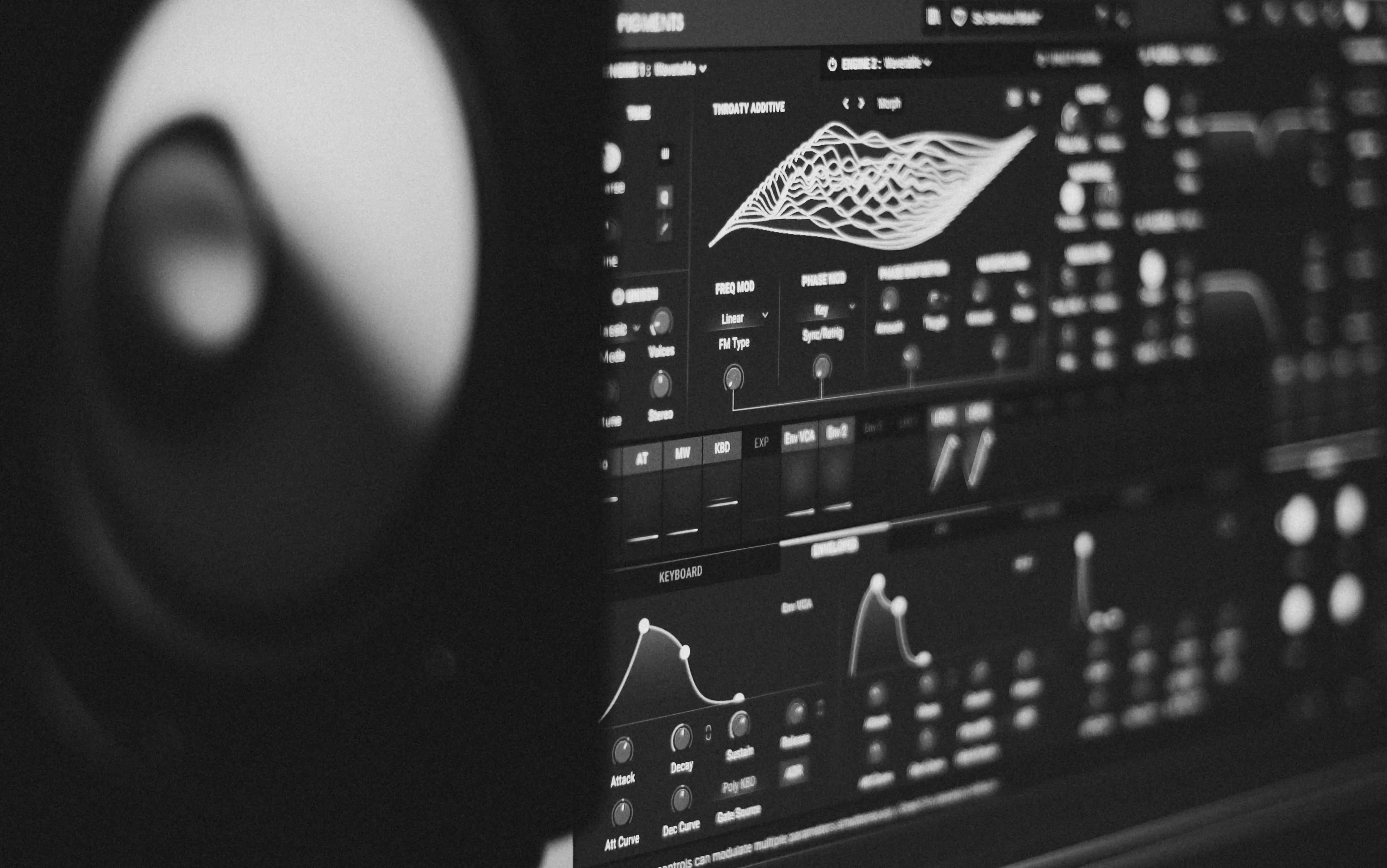 Bildschirm mit der Benutzeroberfläche des Wavetable-Synthesizers Pigments, davor die unscharfe Silhouette eines Studiomonitors, schwarzweiß.